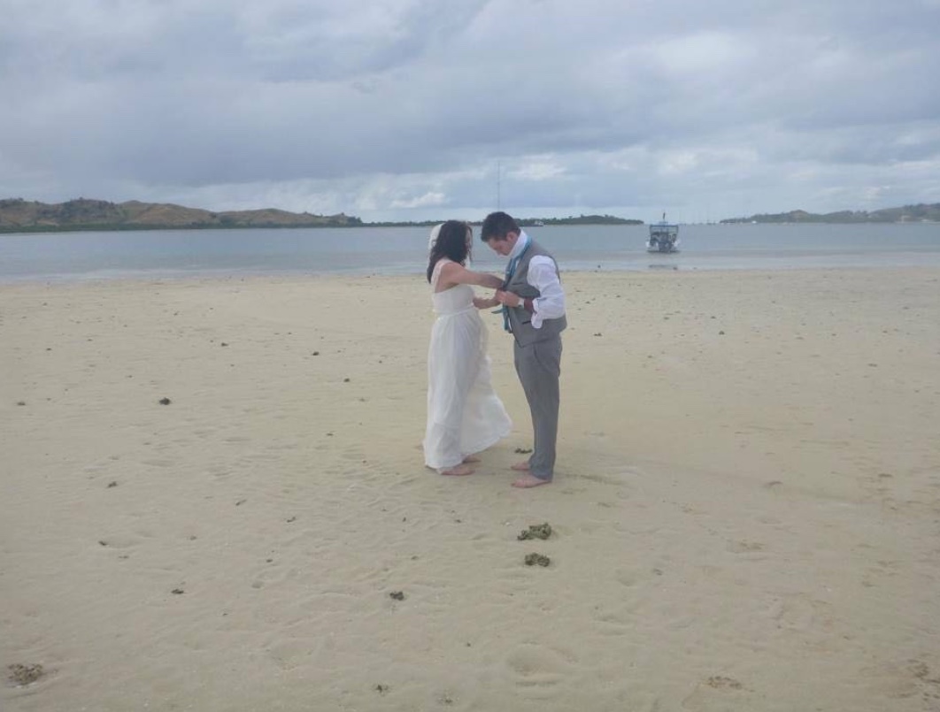 A couple standing on a bare sandbank at low tide, the tour boat waiting in the shallows behind them