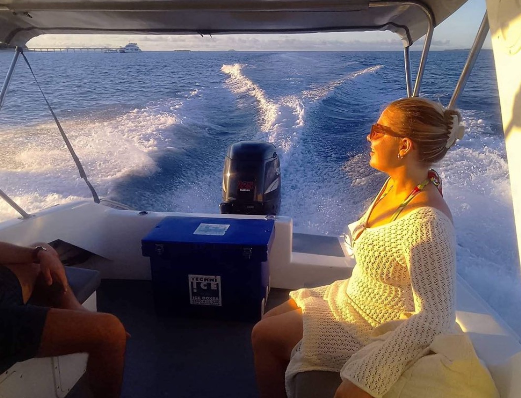 A guest in the stern of the boat in low golden light, the wake spreading out behind her